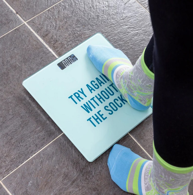 Bilancia pesa persone azzurra con scritta “Try again without the socks” e termometro