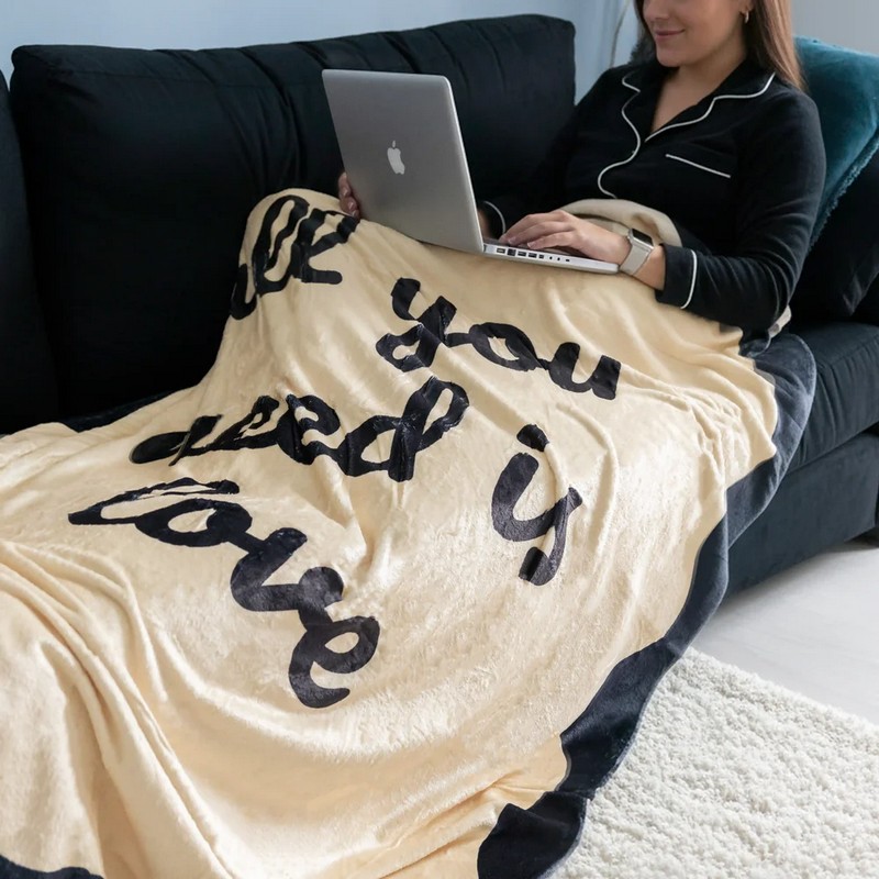 Coperta in flanella color sabbia decorata con bordi neri e scritta “All you need is love”, una caldissima idea regalo Natale o coppie