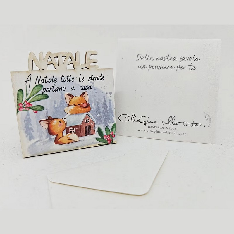 Magnete in legno di betulla con busta inclusa, utilizzabile anche come biglietto, decorato con volpi in paesaggio natalizio e con scritta “A Natale tutte le strade portano a casa”, per un'originalissima idea regalo di Natale