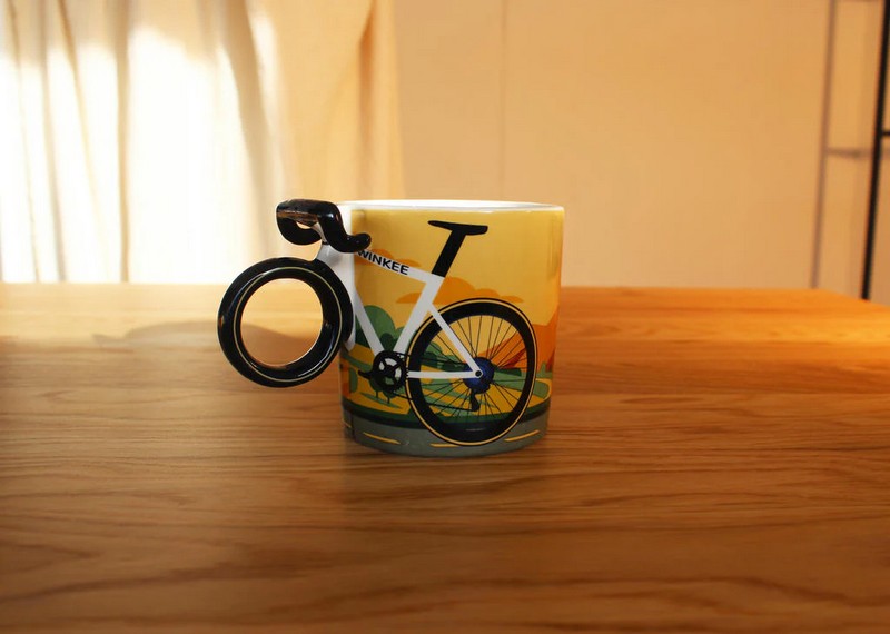 Tazza mug in ceramica con bicicletta da corsa e ruota come manico, decorata con paesaggio e scritta “Enjoy your coffee ride”