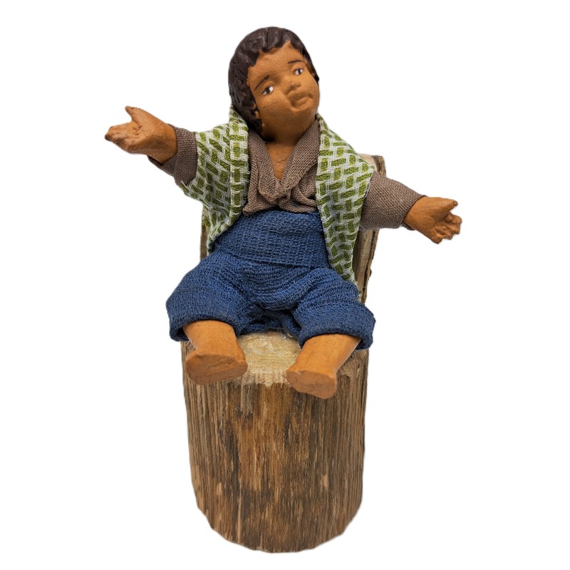 Bambino seduto su un tronco del presepe napoletano, prodotto artigianale della città metropolitana di Napoli fatto a mano e dipinto a mano